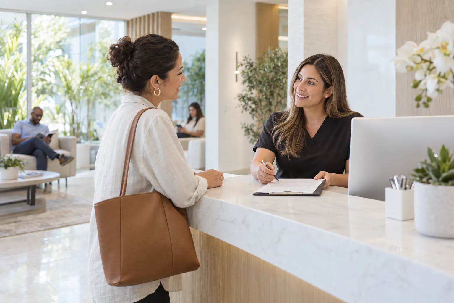 A woman speaks with a receptionist at a bright dental office front desk.